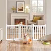 A dog is sitting in front of a white wooden pet gate in a living room with a fireplace and armchair. Podgląd zdjęcia produktu