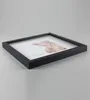 A black square picture frame is shown from a side angle, resting on a light gray surface. Produktbild-Vorschau