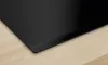A close-up view of a black induction cooktop on a light wooden countertop. Náhľad obrázku produktu