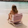 A woman sitting on a beach chair facing the ocean. Produktbild-Vorschau