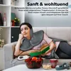 A woman is lying on a couch, reading a book, and wearing a gray heating pad around her neck and shoulders. Produktbild-Vorschau