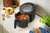 A Russell Hobbs air fryer filled with french fries sits on a kitchen counter next to a plate of food and a bowl of salad. Produktbild-Vorschau