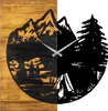 A split image showing a wooden clock with a mountain and forest scene on the left, and a black silhouette of mountains, trees, and a tent on the right. Voir les images du produit