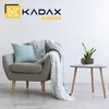 A cozy armchair with a blanket and pillow next to a small side table with a potted plant. Podgląd zdjęcia produktu