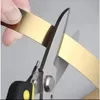 A close-up shot of a hand holding a gold metallic strip while a pair of scissors cuts through it. Podgląd zdjęcia produktu