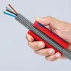 A hand holding a Knipex TwistCut Wellrohrschneider tool, which is cutting through a flexible conduit with wires inside. Voir les images du produit