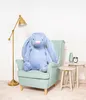 A large blue plush bunny sits in a mint green armchair next to a gold floor lamp and two small side tables. One table has a vase and an alarm clock on it. Podgląd zdjęcia produktu