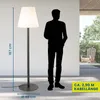 A silhouette of a person stands next to a tall floor lamp, with outdoor furniture visible in the background. Anteprima dell’immagine prodotto