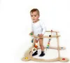 A baby is standing in a wooden baby walker with toys attached. Produktbild-Vorschau