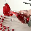 A hand is pouring a red liquid from a glass bottle into a small glass, surrounded by raspberries on a wooden surface. Voir les images du produit