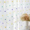 Sheer curtains with colorful pom-pom accents hanging in front of a window. Produktbild-Vorschau