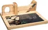 A wooden bread slicer with a stone cutting surface, shown with some bread and herbs. Náhled obrázku produktu