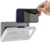 A hand is holding a smartphone with a blue case over a white waterproof phone case attached to a wall. Podgląd zdjęcia produktu