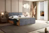 A bedroom scene featuring a large bed with a dark gray upholstered headboard and frame, wooden accents, and a mattress. There are bedside tables with lamps, curtains, and a large window with a view of autumn trees. Produktbild-Vorschau