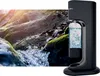 A black soda maker is placed in front of a natural scene of moss-covered rocks and flowing water, suggesting the purity and natural origin of the water used for carbonation. Produktbild-Vorschau