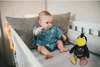 A baby sitting in a crib next to a stuffed toy. Produktbild-Vorschau