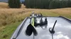 Skis mounted on a car roof rack, with a grassy and wooded landscape in the background. Náhled obrázku produktu