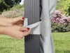 A person's hands are shown securing a light gray curtain to a dark gray pole of a gazebo. Produktbild-Vorschau
