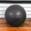 A dark, spherical object sits on a wooden surface in front of a slatted background. Produktbild-Vorschau