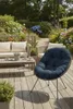 A comfortable outdoor seating area with a blue cushion chair, a sofa, and a coffee table on a wooden deck, surrounded by lush green plants and flowers. Anteprima dell’immagine prodotto