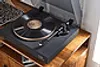 A turntable is placed on a wooden surface. Voir les images du produit