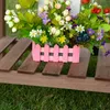 A pink planter box filled with artificial flowers sits on a wooden slatted surface. Produktbild-Vorschau