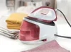 A steam generator iron and folded laundry on a white surface. Produktbild-Vorschau