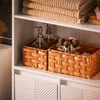 A close-up view of a bathroom shelf with towels stacked on top and woven baskets containing toiletries and makeup brushes below. Náhled obrázku produktu