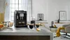 A modern kitchen counter with a black espresso machine, coffee cups, and fruit. Produktbild-Vorschau