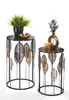 Two decorative metal side tables with leaf motifs, one holding a potted plant and the other a vase with decorative branches and a candle. Produktbild-Vorschau
