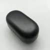 A black oval-shaped object, likely a charging case for earbuds, is shown on a white and light gray textured surface. Voir les images du produit