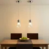 Two pendant lights hang over a dining table with chairs and a bowl of apples. Produktbild-Vorschau