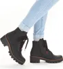 A pair of black lace-up ankle boots with a thick sole, worn by a person wearing light blue cuffed jeans. Produktbild-Vorschau