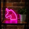 A pink neon unicorn light is displayed on a shelf next to a potted plant. Voir les images du produit