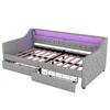 A grey upholstered daybed with wooden slats and two drawers, one of which is pulled out to reveal a wire basket. The headboard has integrated purple ambient lighting. Náhled obrázku produktu