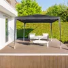 A black gazebo with outdoor furniture set up on a wooden deck, surrounded by lush green hedges and trees. Produktbild-Vorschau