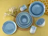 A set of blue ceramic dishes and cups arranged on a yellow textured surface, with some decorative dried grass. Náhľad obrázku produktu