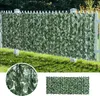 A green artificial hedge fence is installed on a white picket fence in a grassy yard. Náhled obrázku produktu