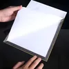 Hands holding a white sheet of paper over a dark surface, revealing a thin frame with a gray border and a gold edge underneath. Anteprima dell’immagine prodotto