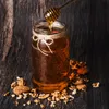 A jar of honey with a honey dipper, surrounded by walnuts on a wooden surface. Produktbild-Vorschau