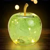 A green glass apple with embedded LED lights sits on a wooden surface. Voir les images du produit