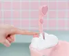 A hand is pressing a button on a pink toy bathtub with a heart-shaped shower head. Produktbild-Vorschau