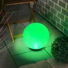 A green illuminated sphere sits on a tiled patio next to a small bush and a wooden chair. Produktbild-Vorschau