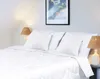 A neatly made bed with white bedding and pillows, illuminated by bedside lamps. Podgląd zdjęcia produktu