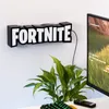 A Fortnite logo light mounted on a white wall, with a computer monitor and a plant in the foreground. Anteprima dell’immagine prodotto