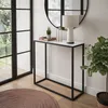 A modern console table with a marble top and black metal frame, decorated with a lamp, a small plant, and candles. It is placed in a well-lit room with large windows and a round rug. Produktbild-Vorschau
