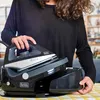 A person is holding a steam iron over its base station. Produktbild-Vorschau
