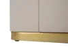 A close-up view of the bottom section of a cabinet or nightstand, showing its textured cream-colored surface and a gold-colored base. Náhled obrázku produktu