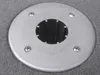A close-up view of a circular metal mounting plate with a central opening, screwed into a grey carpeted surface. Produktbild-Vorschau