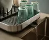 A dish rack with glasses and a plate, placed over a sink with water draining. Voir les images du produit
